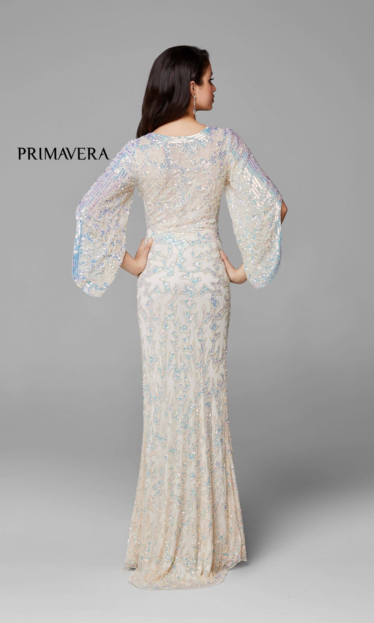 A woman faces away from the camera in a Long Bell Sleeve Beaded Evening Gown 9713 with a fitted waist, floor-length silhouette, and sheer beadwork.